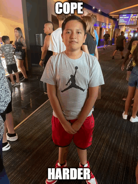 a young boy wearing a grey jordan shirt stands in a crowded room with the caption cope harder