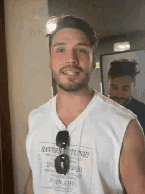 a man with a beard wears a white tank top that says raves hotline