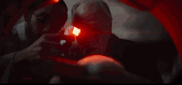 a man is holding a red light in his hand while another man looks at it .