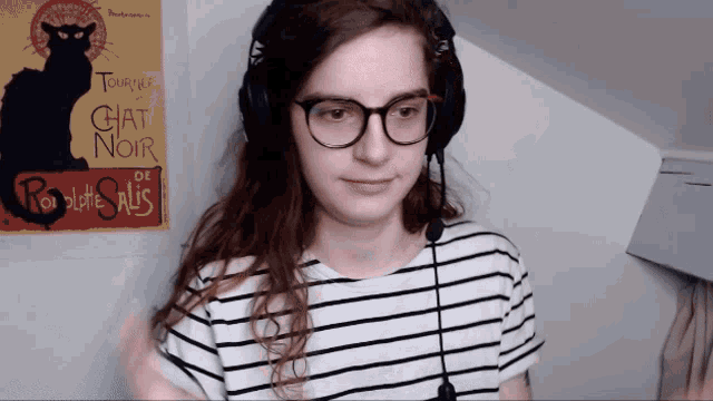 a woman wearing glasses and headphones stands in front of a poster that says chat noir