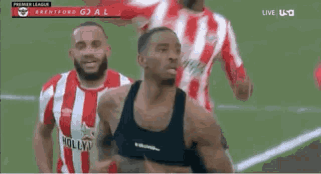 a man in a black tank top is running on a soccer field with other players .