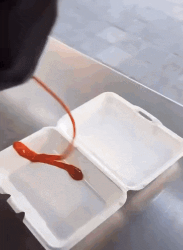 ketchup is poured into a styrofoam container on a table