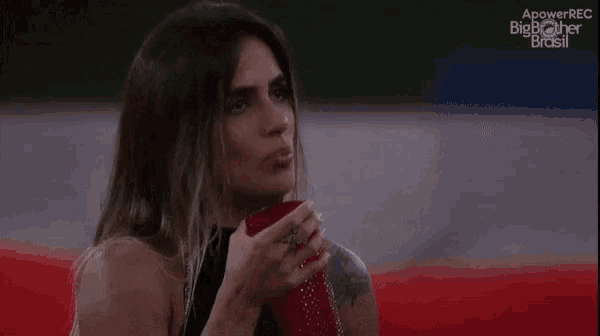 a woman is drinking from a red cup and the words big brother brasil are on the screen