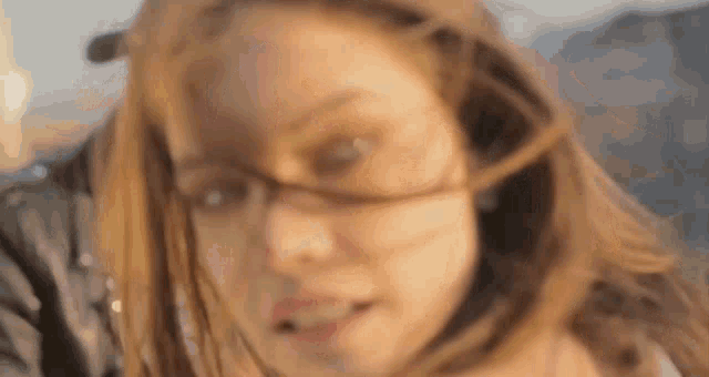 a close up of a woman 's face with glasses and long hair blowing in the wind .