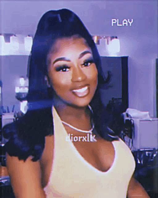 a woman in a yellow tank top is smiling in front of a play sign on the wall