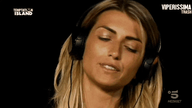 a woman wearing headphones is watching temptation island on tv