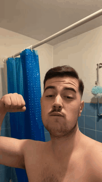 a shirtless man in a bathroom with a blue shower curtain