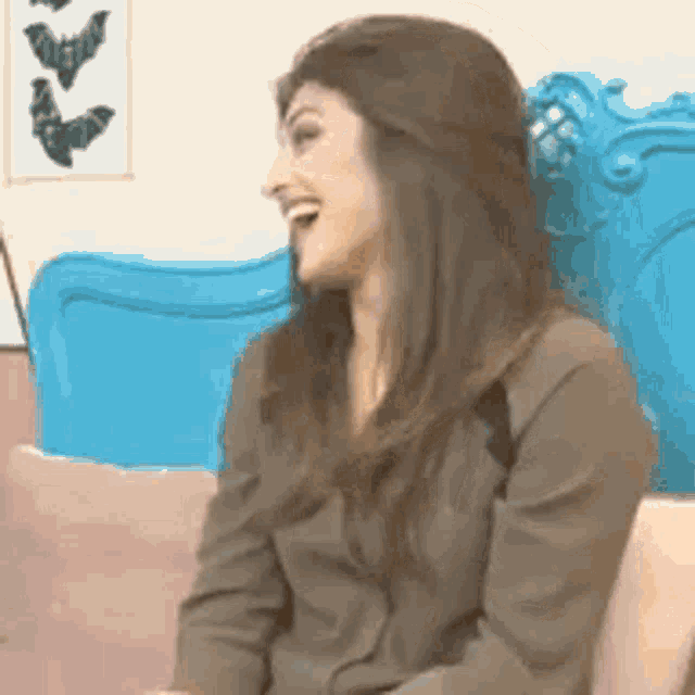 a woman is sitting on a blue couch laughing and smiling .