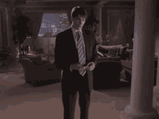 a man in a suit and tie is standing in a living room looking at his phone