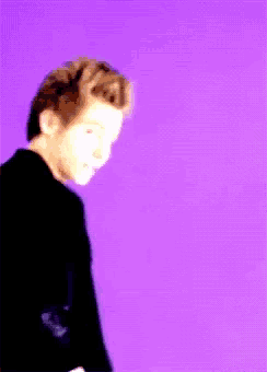 a man in a black jacket is standing in front of a purple wall