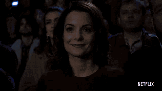 a woman is smiling in a crowd of people while sitting in a theatre .