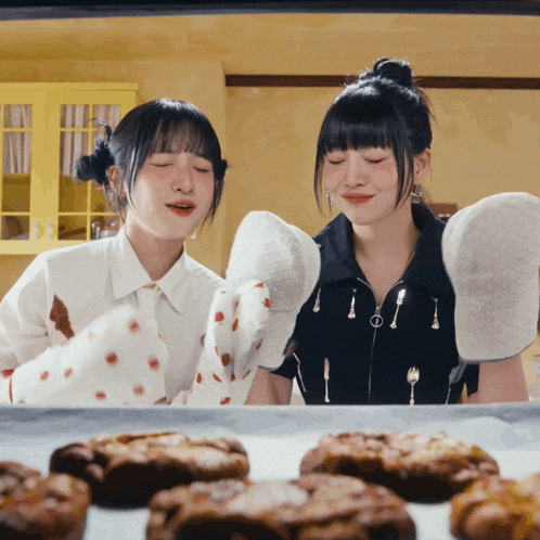 two girls wearing oven mitts looking at a pan of cookies