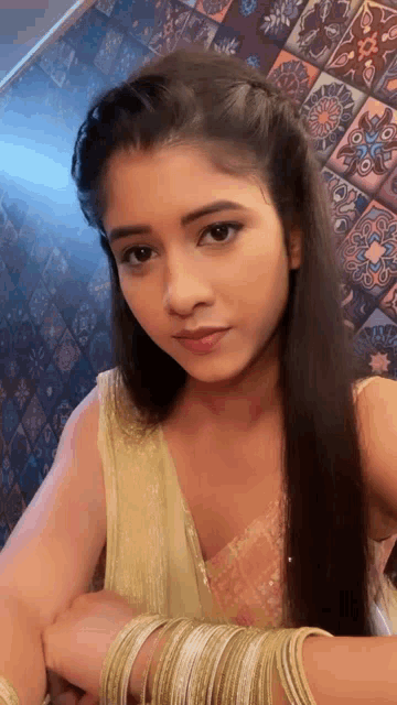 a woman with long hair is wearing a gold dress and bracelets .