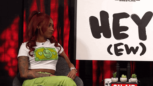 a woman sits in front of a sign that says hey ew