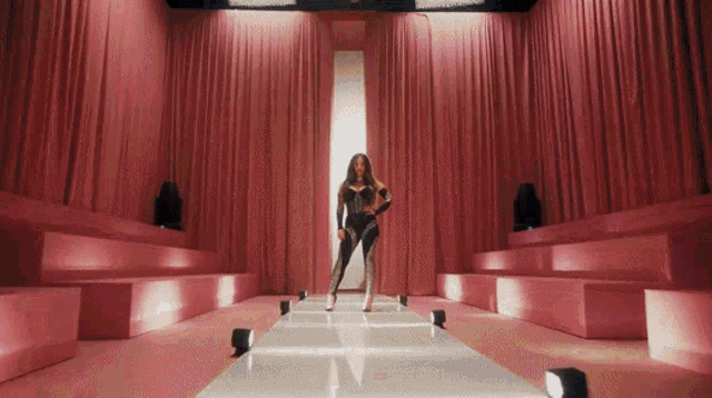 a woman walking down a runway with pink curtains