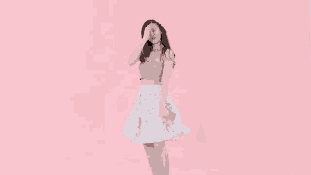a woman in a pink top and a white skirt is standing in front of a pink background .