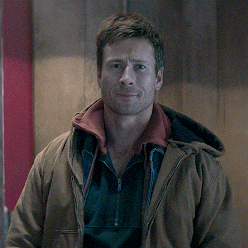 a man wearing a brown jacket with a red collar is smiling