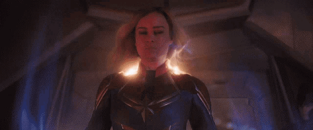a woman in a captain marvel costume is standing in a dark room with a star on her chest .