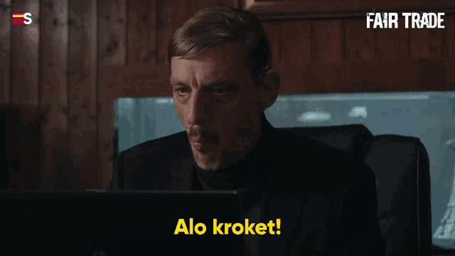 a man sitting in front of a laptop with the words " alo kroket " on the bottom right