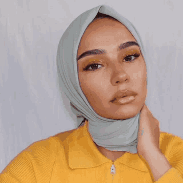 a woman wearing a pink hijab and a blue shirt looks at the camera