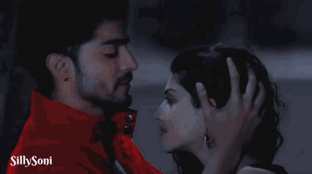 a man in a red jacket is touching a woman 's forehead with a silly soni logo in the corner