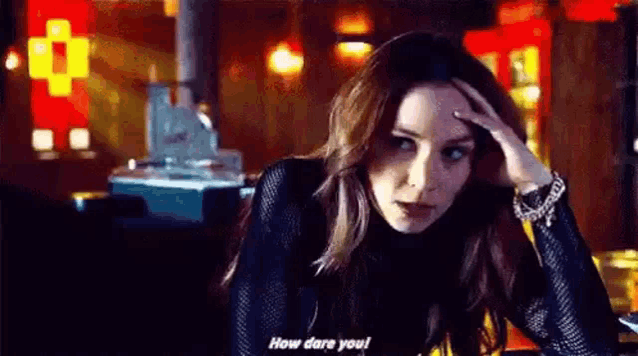 a woman is sitting at a table with her hand on her forehead and saying `` how dare you '' .