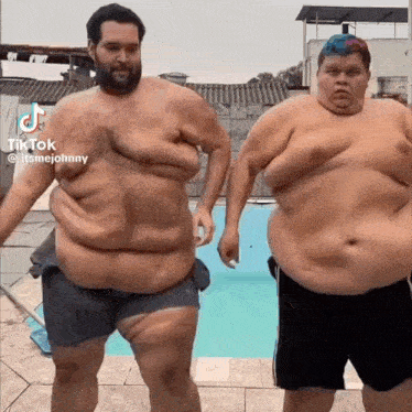 two very fat men are standing next to each other by a pool .