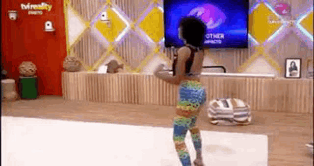 a woman in colorful pants is dancing in front of a tv .