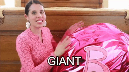 a woman in a pink shirt is holding a large pink balloon that says giant on it