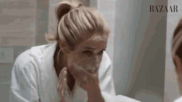 a woman washing her face in front of a mirror with the word bazaar on the bottom