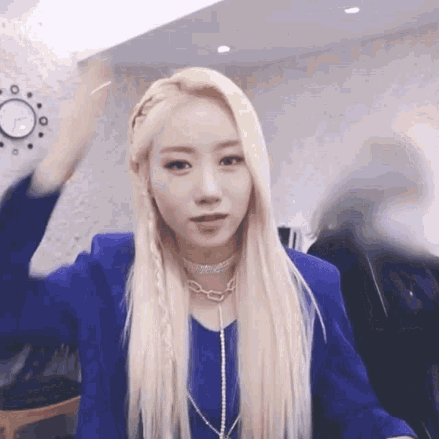 a woman with blonde hair is wearing a blue jacket and necklace .