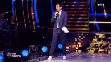 a man in a suit stands on a stage holding a microphone and a piece of paper in his hand .