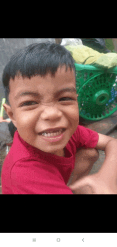 a young boy in a red shirt is smiling for the camera while sitting next to a green basket .