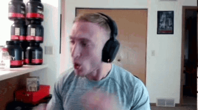 a man wearing headphones is making a funny face in front of a stack of protein bottles .