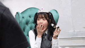 a girl wearing a tiara is sitting in a chair with her mouth open and holding a bottle .