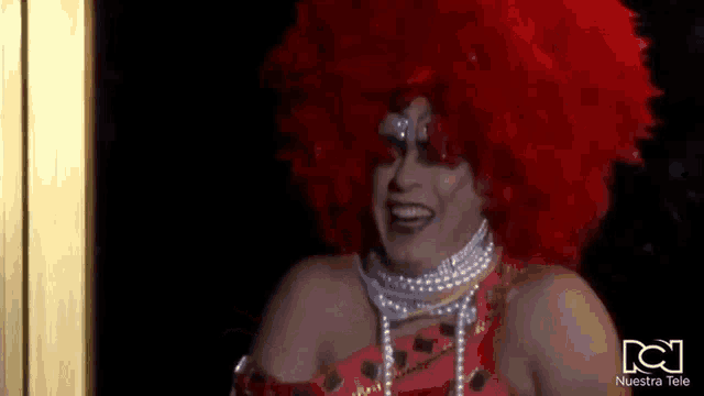 a drag queen with a red wig and pearls is smiling .