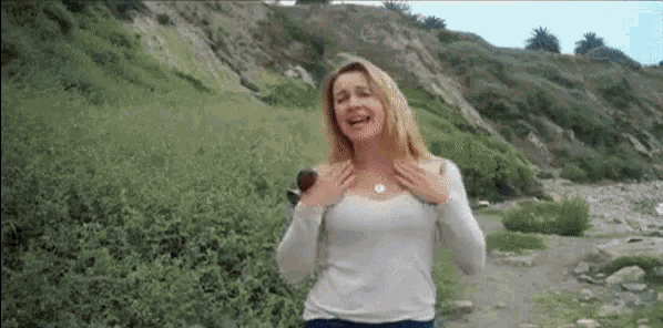 a woman in a white shirt is standing in a field with her hands on her breasts .