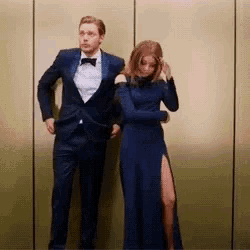 a man in a suit and tie is standing next to a woman in a blue dress in an elevator .