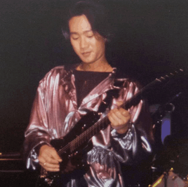 a man in a silver jacket is playing a guitar in a dark room