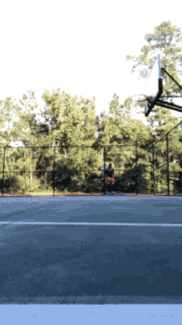 a person is playing basketball on a court with a fence in the background