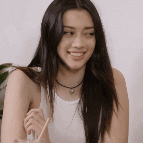 a woman wearing a choker and a white tank top smiles for the camera