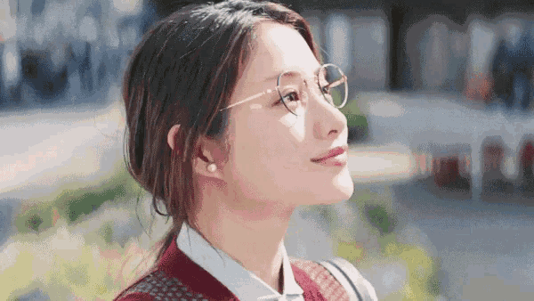 a woman wearing glasses and a red sweater is looking up at the sky .