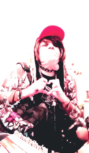 a person wearing a red hat and a choker making a heart shape with their hands