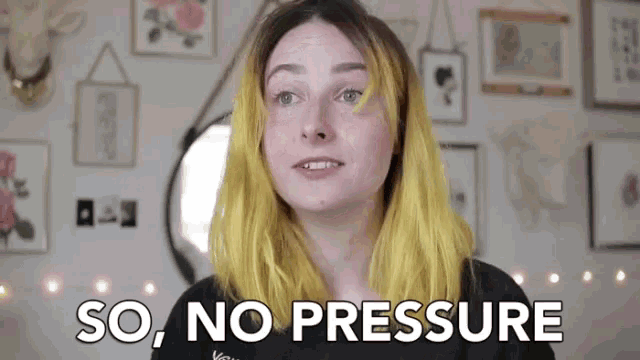 a woman with yellow hair is standing in front of a wall with paintings and says `` so , no pressure '' .