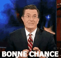 a man in a suit and tie says " bonne chance " in front of a blue background