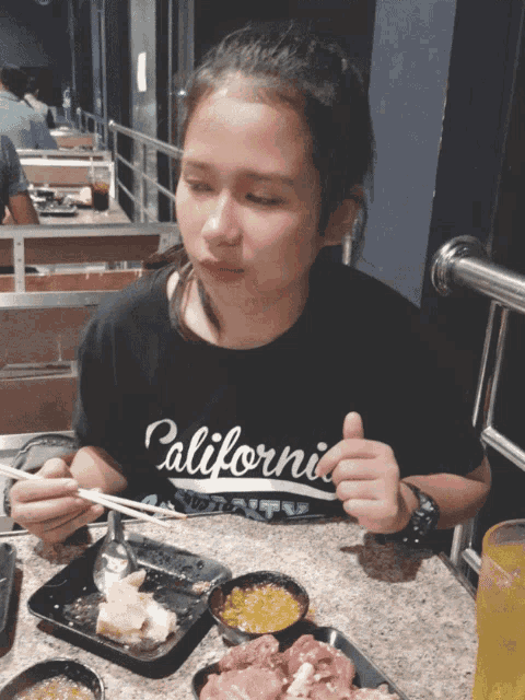 a girl wearing a black shirt that says california is eating food with chopsticks