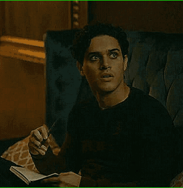a man is sitting in a chair reading a book while holding a pen .