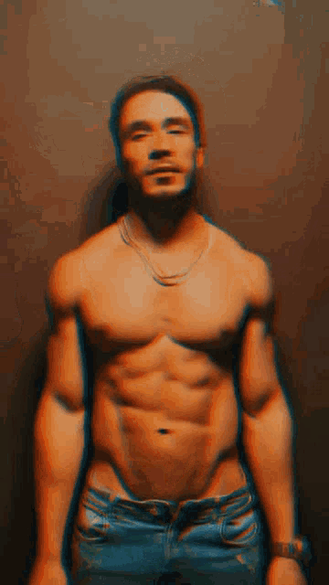 a shirtless man wearing jeans and a necklace