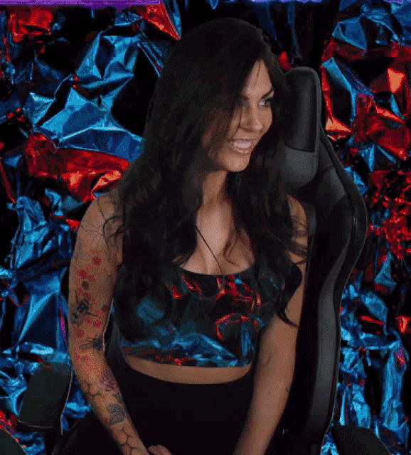 a woman in a crop top is sitting in a chair in front of a blue and red background