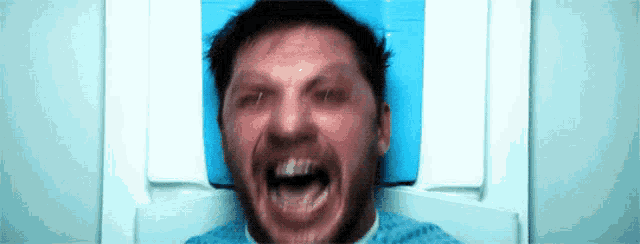 a man is laying in a hospital bed with his mouth open and screaming .